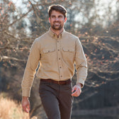 A man in a Tom Beckbe Hartwell Moleskin Shirt and brown pants walks outdoors on a sunny, tree-lined day.