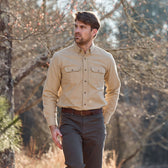 A man in a Tom Beckbe Hartwell Moleskin Shirt and dark pants walks outside among trees and dry grass.