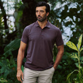 A man in the Tom Beckbe Hutton Performance Polo and beige shorts stands outdoors among green plants with a neutral expression.