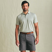 Man wearing a Tom Beckbe Hutton Performance Polo, brown belt, and dark gray shorts against a plain background.