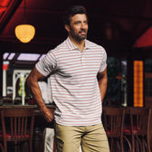 Man indoors wearing Tom Beckbe Hutton Performance Polo in white/red stripes and khaki pants, hands in pockets.