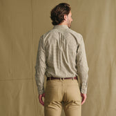 Man standing with his back to the camera, wearing a checked shirt and khaki pants against a plain beige background.