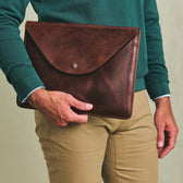 A person holds a Tom Beckbe Leather Portfolio, wearing a green shirt and tan pants.
