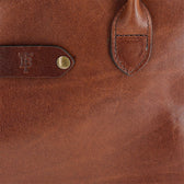 Close-up of Tom Beckbes Palmer Leather Tote, featuring embossed logo, strap, and brass button detail on the front.