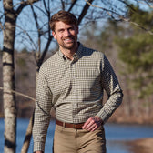 A man in a Tom Beckbe Knapp Cotton Twill Shirt walks outdoors by trees and water on a sunny day.