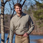A man in a Tom Beckbe Knapp Cotton Twill Shirt walks outdoors by trees and water on a sunny day.