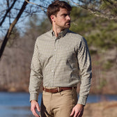 Man wears a Tom Beckbe Knapp Cotton Twill Shirt and khaki pants outdoors by water and trees.