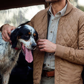 Man in a tan Tom Beckbe Logan Bomber Jacket with a black and white dog, dog panting, mans face not visible.