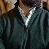A man wearing a dark green Tom Beckbe York Merino Quarter Zip over a white checkered collared shirt.