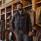 A man in a brown jacket stands in a store with wooden shelves displaying Tom Beckbe York Merino Quarter Zips.