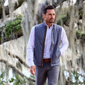 A man in a Monroe Poplin Shirt by Tom Beckbe strolls outdoors in classic fit gray vest and pants near mossy trees.