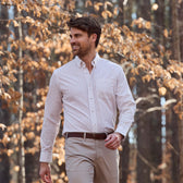 Man in a Tom Beckbe Monroe Poplin Shirt and khaki pants walks outdoors among trees and brown leaves.