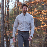 A man in a Tom Beckbe Monroe Poplin Shirt and gray pants walks outdoors among autumn leaves.