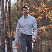 Man wearing a Tom Beckbe Monroe Poplin Shirt and gray pants walking outdoors among autumn forest foliage.