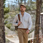 Man walking outdoors in a Tom Beckbe Monroe Poplin Shirt with khaki pants, a backpack, and hammock among the trees.