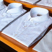 Monroe Poplin Shirts by Tom Beckbe are neatly folded and displayed on a wooden shelf in the clothing store.