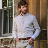 Man in a Monroe Poplin Shirt and beige pants stands by a wooden building, hands in pockets, exuding classic fit style.