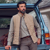 A man in a Monroe Poplin Shirt by Tom Beckbe leans against a blue SUV with travel bags in the back.