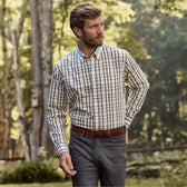 Wearing a Monroe Poplin Shirt by Tom Beckbe and gray pants, a person walks through a tree-lined forest.
