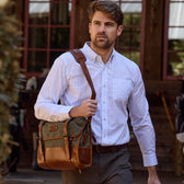 A man in a classic fit Tom Beckbe Monroe poplin shirt and green pants carries a satchel, standing before a building.