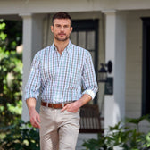 A man in a Tom Beckbe Monroe Poplin Shirt and beige pants confidently walks past a white house with a porch.