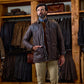 A man in a Tom Beckbe Paddock Quilted Jacket and beige pants stands in a store with weatherproof jackets behind him.