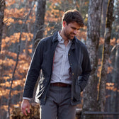Man wearing a Tom Beckbe Piedmont Jacket and checked shirt stands outdoors among autumn leaves in the woods.