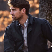 Man with short brown hair and beard in a Tom Beckbe Piedmont Jacket and checked shirt, looking left outdoors.