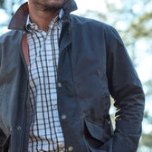 A person in a Tom Beckbe Piedmont Jacket over a plaid shirt stands outdoors with trees blurred in the background.