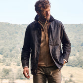 A man in a Tom Beckbe Piedmont Jacket stands outdoors with a mountainous backdrop.