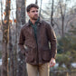 A man wears a Tom Beckbe Piedmont Jacket, green shirt, and tan pants while standing outdoors with hands in pockets.