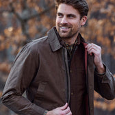 Man outdoors in a Tom Beckbe Piedmont Jacket over a plaid shirt, smiling and adjusting his collar.