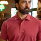 Man with a beard wearing a red polo shirt stands indoors, looking to the side with a neutral expression.