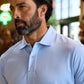 Man with a beard wearing a light blue polo shirt indoors, with blurred background.