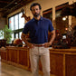A man in a navy polo shirt and beige pants stands indoors in a store with wood counters and mounted animal heads on the walls.