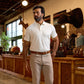 A man in a white polo shirt and beige pants stands in a rustic store with animal mounts and leather bags in the background.