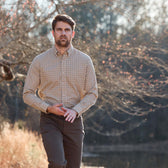 A man wears the Tom Beckbe Knapp Cotton Twill Shirt with dark pants while walking outdoors by trees and water on a sunny day.