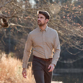 A man in the Tom Beckbe Knapp Cotton Twill Shirt and dark pants walks outdoors near trees, looking off to the side.