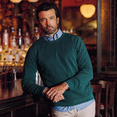 A man in a Tom Beckbe Foley Pima Crewneck Sweater stands by a bar, looking at the camera with a neutral expression.
