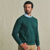 Man wearing the Tom Beckbe Foley Pima Crewneck Sweater over a light blue shirt and tan pants against a plain background.