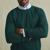 Man with folded arms wearing Tom Beckbe's Foley Pima Crewneck Sweater in green over a white checkered shirt.