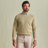 Man stands against a plain background in a Tom Beckbe Foley Pima Crewneck Sweater over a checkered shirt and light pants.