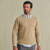 Man wearing the Tom Beckbe Foley Pima Crewneck Sweater over a collared shirt with gray pants, set against a beige background.