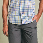 A person wears a Tom Beckbe Powell Performance Shirt (Short Sleeve) and gray shorts, standing with one hand in a pocket.