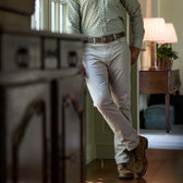 Person in a checkered shirt and Tom Beckbe Reid Straight Leg Cotton Chino Pant leans on a windowsill in a cozy room.
