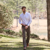 Man wearing Tom Beckbe Reid Straight Leg Cotton Chino Pant outdoors on grass with trees in the background.
