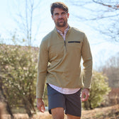 Man in a light brown quarter-zip pullover and Tom Beckbes Reid Short strolls outside in a spring setting with trees.