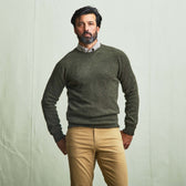 Man with dark hair and beard wears the Tom Beckbe Saunders Crewneck Sweater in green, beige shirt, and tan pants.