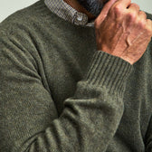 A person in a green Tom Beckbe Saunders Crewneck Sweater rests their hand on their chin, face partly out of frame.