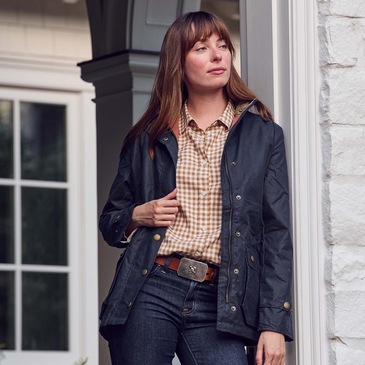 Woman in a dark jacket and Tom Beckbe Womens Smyth Cotton Twill Shirt stands by a white brick wall and window.